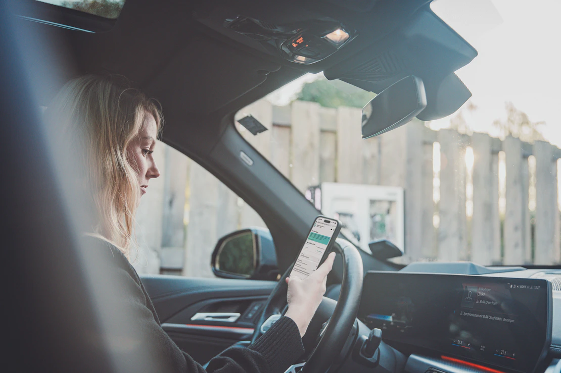A woman uses the Charge Repay Service from Phoenix Contact on the smartphone in a parked car.